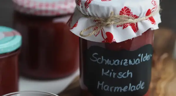 Glas mit hausgemachter Kirschmarmelade, beschriftet mit "Schwarzwälder Kirsch Marmelade". Ein tolles Rezept für den Sommer!