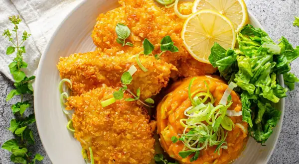 Knuspriges Zucchin Schnitzel mit Kürbispüree, Salat und Zitronenspalten.