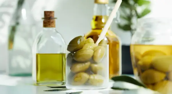 Zielone oliwki w szklance i butelkach z oliwą. Czy oliwa z oliwek jest kaloryczna? Tak, jest, ale zdrowa!