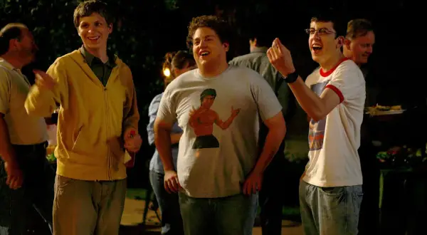 Die Besetzung von Superbad feiert eine Party. Michael Cera, Jonah Hill mit Bruce Lee T-Shirt und Christopher Mintz-Plasse lachen ausgelassen.