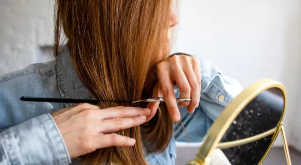 Frau schneidet sich mit Schere und Kamm die Haare, wie in einer stufenschnitt anleitung bilder.