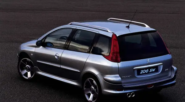 Srebrny Peugeot 206 SW z relingami dachowymi i podwójnym wydechem, zaparkowany na ciemnym asfalcie.