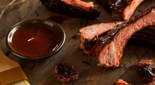 Soczyste żeberka w sosie BBQ, obok miseczka z marynatą do żeberek i pędzelek.