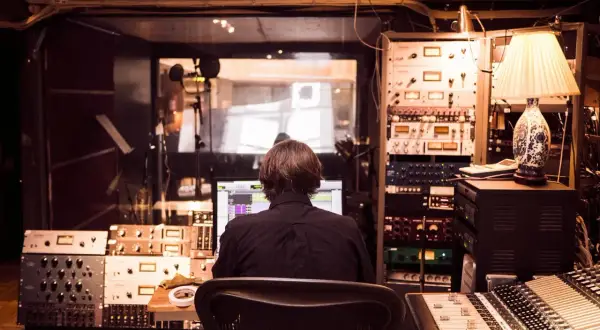 Producent muzyczny w studio, otoczony sprzętem, tworzy nową muzykę, być może z pomocą sztucznej inteligencji.