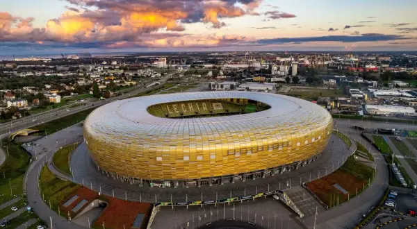 Stadion Energa w Gdańsku, znany jako Letnica Gdańsk, lśni złotem pod zachodzącym słońcem.