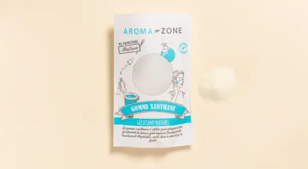 Un sachet de gomme xanthane Aroma-Zone, un gélifiant naturel pour vos cosmétiques maison. Une poudre fine à côté du paquet.