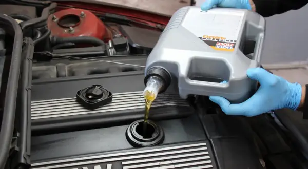 Ręce w niebieskich rękawiczkach wlewają olej silnikowy Liqui Moly do silnika. Czy można mieszać oleje silnikowe? To pytanie nurtuje wielu kierowców.