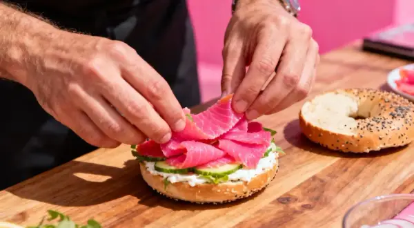 Préparation d'un bagel garni de saumon fumé, de fromage frais et de concombre. Un accompagnement bagel parfait pour un brunch.