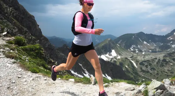Kobieta w sportowym stroju biegnie po górskim szlaku, ciesząc się pięknem krajobrazu. To prawdziwe bieganie po górach!