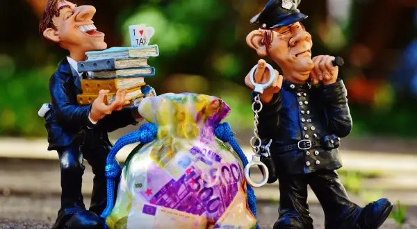 Figurki: uradowany mężczyzna z książkami i kubkiem "I LOVE TAX" obok policjanta z kajdankami i torbą pieniędzy. To poświadczenie nieprawdy przykłady.