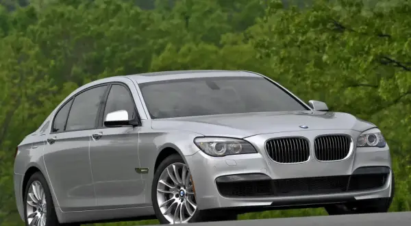 Srebrne BMW 7 F01 na tle zielonych drzew. Elegancka limuzyna prezentuje się okazale na drodze.
