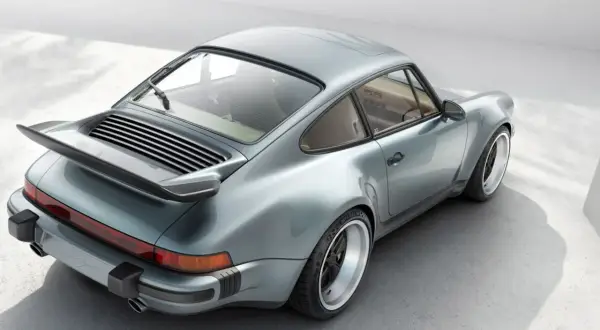 En ikonisk Porsche 80-tals coupé i ljusblått, med sin karaktäristiska bakvinge och breda fälgar.