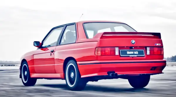 Czerwone BMW E30 Coupe M3 w ruchu, z widocznym spojlerem i podwójnym wydechem.