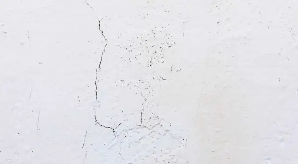 Biały tynk z widocznymi pęknięciami i drobnymi nierównościami.