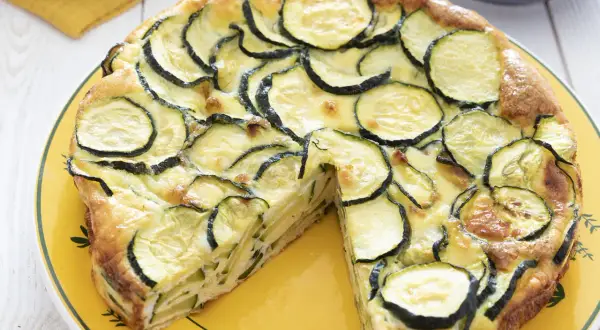 Une délicieuse frittata courgette, garnie de rondelles de courgettes fraîches et dorées, servie sur une assiette jaune.