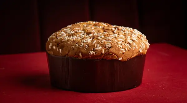 Un panettone tradicional, uno de los tipos de panettone, cubierto con azúcar perlado y almendras, sobre un mantel rojo.