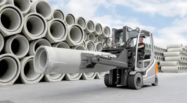 Wózek widłowy z operatorem transportuje dużą betonową rurę. W tle piętrzą się kolejne elementy tej jednostki ładunkowej.