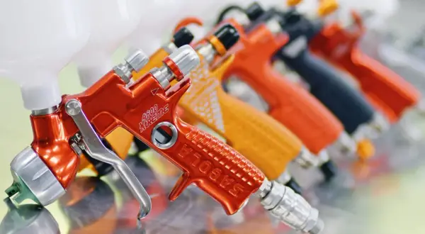 Rząd kolorowych pistoletów lakierniczych, w tym pomarańczowy z napisem "4600 Xtreme". Ustawienia pistoletu lakierniczego są kluczowe dla precyzyjnego malowania.