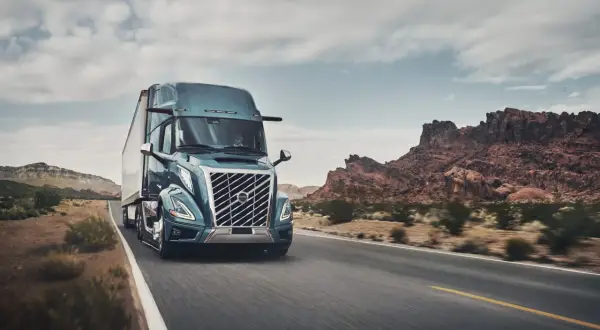 Un camion Volvo américain bleu foncé roule sur une route désertique sous un ciel nuageux.
