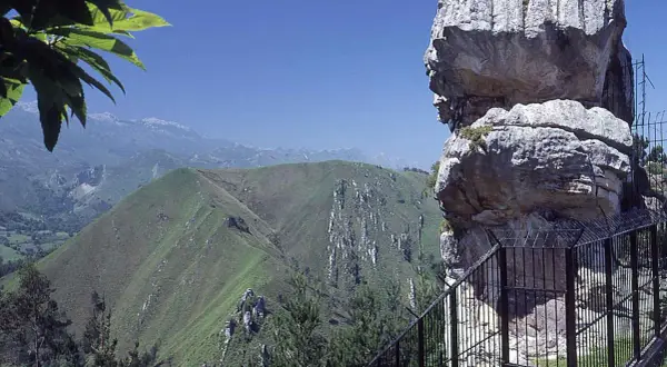 El idolo de peña tu, una roca con forma de perfil humano, vigila un paisaje montañoso verde y sereno bajo un cielo azul.
