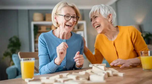 Deux femmes âgées rient en jouant au Jenga, une activité maison de retraite pleine de joie et de complicité.