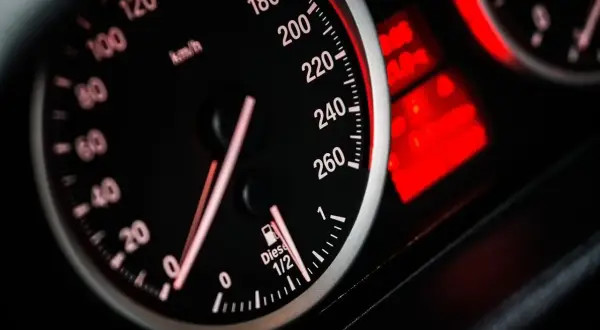 Zbliżenie na deskę rozdzielczą samochodu. Prędkościomierz pokazuje ok. 60 km/h. Wskaźnik paliwa jest na 1/2. Dowiedz się, jak obliczyć spalanie paliwa na 100 km.