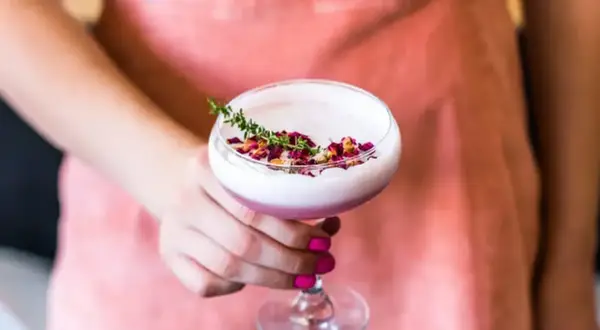 Eleganckie drinki z różowym ginem, ozdobione płatkami róż i gałązką tymianku, prezentowane na tle łososiowego fartucha.