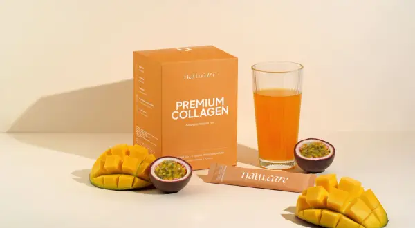 Pudełko z napisem "PREMIUM COLLAGEN Naturalny kolagen rybi", szklanka z pomarańczowym napojem, kawałki mango i marakui.
