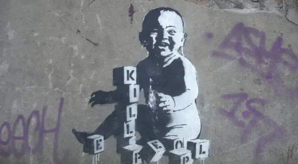 Dziecko bawi się klockami z literami, tworząc napis "KILL". To mocne co to jest graffiti, które prowokuje do myślenia.