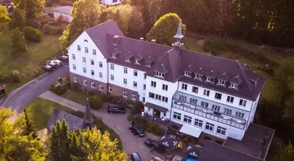 Luftaufnahme des Klosters Ommerborn mit seinem markanten Turm, umgeben von Bäumen und einem Poolbereich.