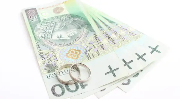 Dwa obrączki na stosie banknotów 100 zł. Symbolizuje to finansowe aspekty małżeństwa, co to jest intercyza.