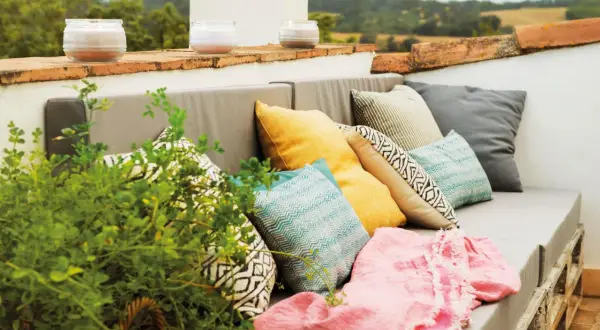 Sofá de palets con cojines coloridos y manta rosa, perfecto para una decoración chill out interiores. Velas aromáticas en la barandilla.