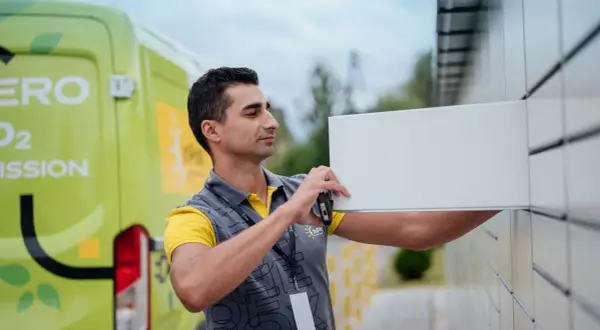 Kurier z zielonego vana z napisem "Zero Emission" wkłada paczkę do paczkomatu. Zastanawiasz się, ile zarabia kurier?