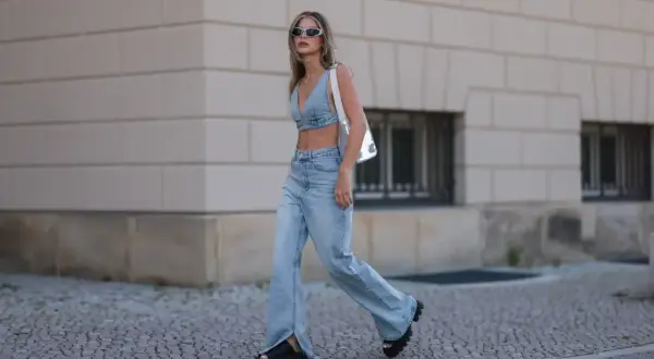 Modna kobieta w jeansach bootcut i denimowym topie, z białym przezroczystym plecakiem. Stylowe jeansy bootcut stylizacje.
