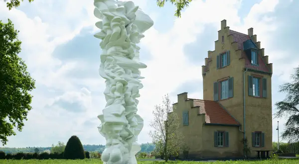 Weiße, organische Skulptur vor einem gelben Gebäude im Freien.