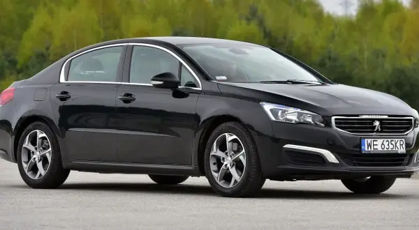 Elegancki, czarny Peugeot 508 z chromowanymi detalami i felgami stoi na tle zieleni.