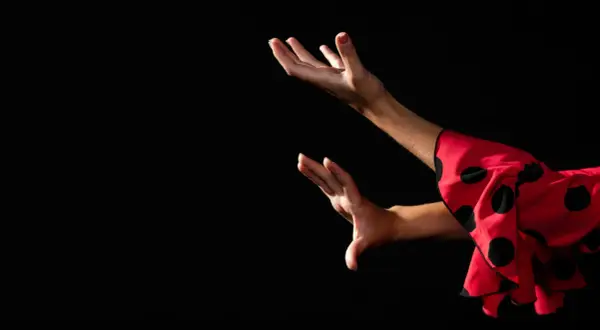 Manos expresivas de una bailaora de flamenco español, con un vestido rojo de lunares negros.