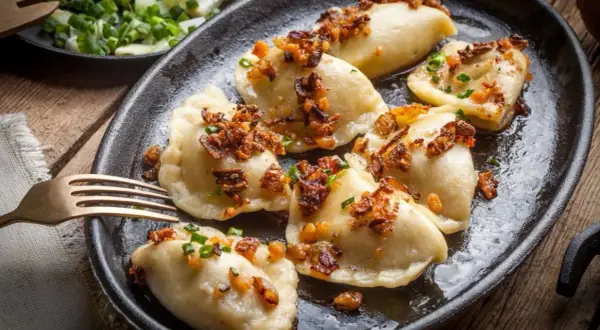 Pyszne pierogi z farszem na pierogi z mięsem mielonym, posypane skwarkami i szczypiorkiem, na czarnym talerzu.