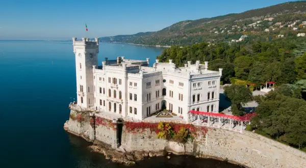Vitt slott vid havet i Trieste, Italien, med en italiensk flagga på tornet.