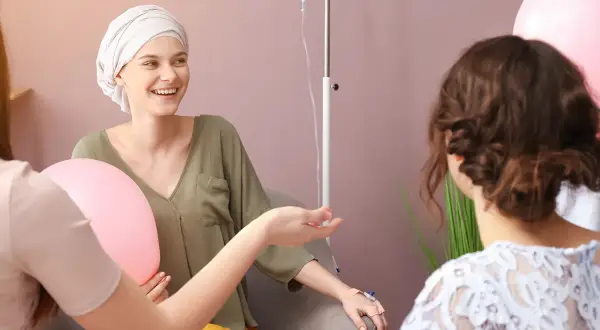 Freundinnen geben einer Frau mit Krebs während der Chemotherapie aufmunternde Worte und halten Ballons.
