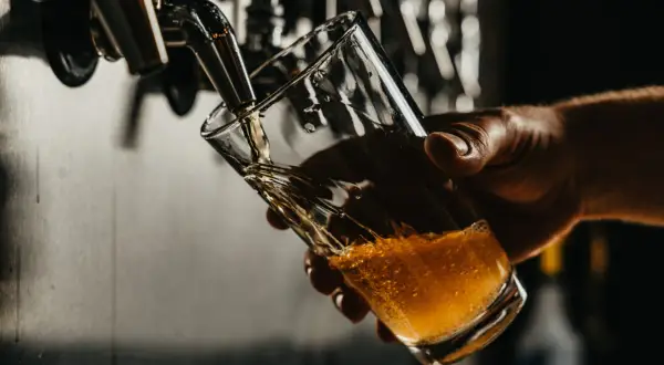 Una mano tiene un bicchiere mentre la birra dorata viene spillata. La temperatura birra è perfetta per gustare questa bevanda rinfrescante.