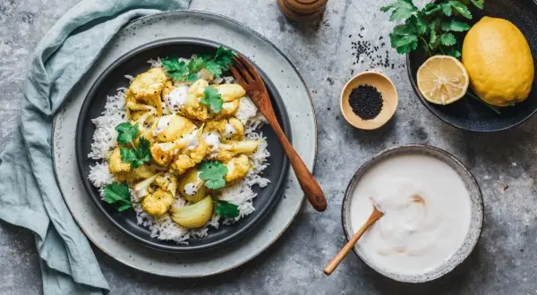 Würziges Karfiol-Rezept mit Reis, garniert mit Koriander und Tahini-Sauce. Dazu Zitrone und schwarzer Sesam.