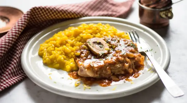 Un piatto di ossobuco ricetta originale con risotto giallo zafferano, guarnito con prezzemolo e scorza di limone.