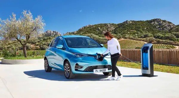 Une femme branche sa Renault Zoé bleue à une borne de recharge. Le temps de recharge zoe 22kw est rapide, parfait pour profiter du paysage.