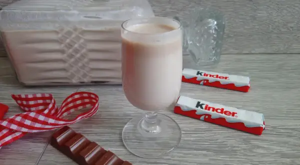 Pyszny likier z kinder czekoladek w kieliszku, obok batoniki i kawałek czekolady.