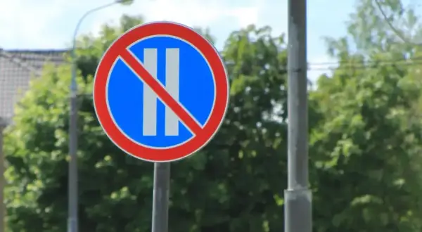 Znak drogowy: zakaz postoju. Dwa pionowe białe paski na niebieskim tle, przekreślone czerwoną linią.