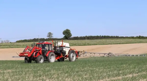 Czerwony traktor z opryskiwaczem polowym pracuje na polu. Tabela mieszania oprysków pomaga rolnikowi w precyzyjnym zabiegu.