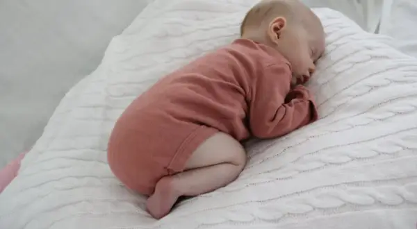 Sover sött på en vit stickad filt, en liten bebis i en rosa body. Hoppas bebisen inte hosta.