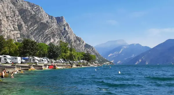 Malowniczy camping nad jeziorem Garda, z kamperami przy brzegu i górami w tle.