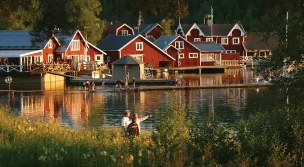 Solnedgång över Norrfjällsviken med röda sjöbodar och folk som njuter av kvällen vid vattnet.